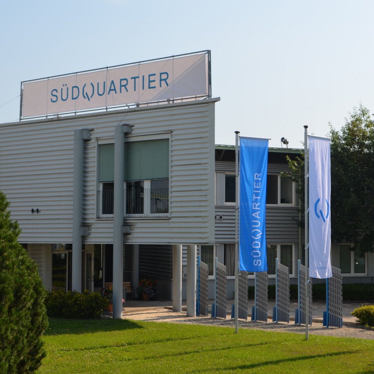 Außenansucht des Standorts "Das SüdQuartier" mit blauen Fahnen mit dem Schriftzug "Das SüdQuartier" vor dem Eingang