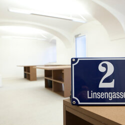 Innenaufname der Location Anlagestelle. Auf einem Tisch steht ein Schild mit der Adresse/Hausnummer "2 Linsengasse"